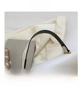 Detail of white faux leather bag handle with precise stitching and gold metal hardware