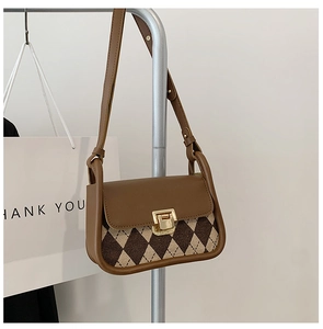 Detail of vintage plaid saddle bag featuring brown leather flap and golden metal clasp buckle