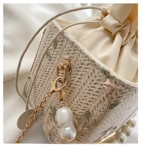 Vue détaillée du crochet doré et de la chaîne en perles sur un sac seau en paille