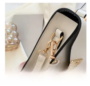 Detailed view of the gold-tone metal hook and black oil-edge finish on the white leather bag