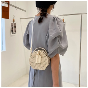 Detailed shot of round straw bag with floral embroidery and white leather straps