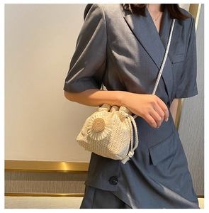 Detail of hand-woven straw bucket bag with floral accent and thin crossbody strap