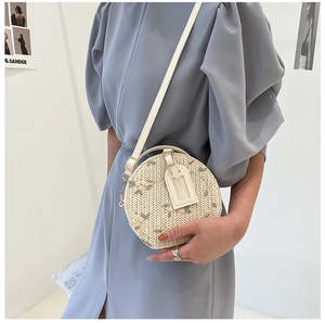 Detail shot of a round woven straw bag featuring floral embroidery and white leather strap