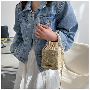 Gros plan du sac seau tissé beige avec broderies florales et anse perlée élégante
