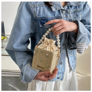 Détail du sac seau en paille avec broderie de fleurs roses et anse en perles