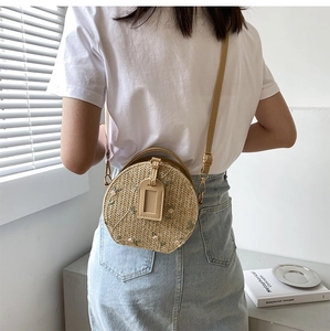 Close-up of a small round straw crossbody bag with delicate floral embroidery details