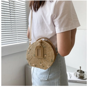 Close-up of a round straw crossbody bag featuring delicate pink flower embroidery details