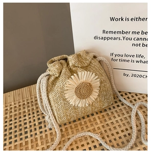Detail of woven straw crossbody bag featuring a large white 3D daisy and cotton drawstring