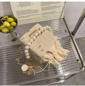 Détail du sac seau en paille avec broderie florale, anse perle et chaîne dorée