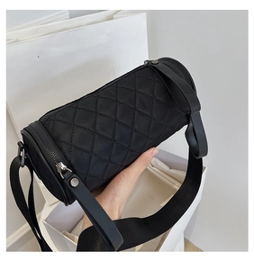 Close-up of black quilted nylon cylinder bag with adjustable strap on white gift box