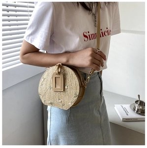 Close-up of a straw woven round crossbody bag with floral embroidery and leather trim