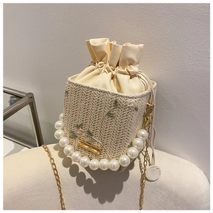 Détail du sac seau en paille avec broderie florale, anse perle et chaîne dorée