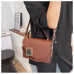 Brown crossbody bag featuring a golden buckle and woven chain detail worn by a model
