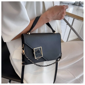 Detail of a black leather handbag with geometric gold buckle and chain strap for women
