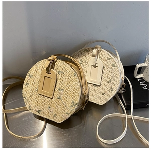 Detail of round straw woven bag featuring delicate floral embroidery and leather tag