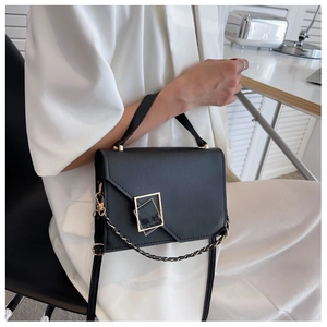 Detail of black leather handbag with gold geometric buckle and braided chain strap