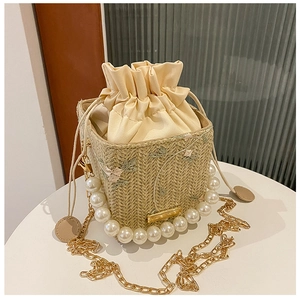 Détail du sac seau en paille avec broderies florales, anse en perles et chaîne dorée