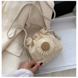 Detail of hand-woven straw bucket bag featuring a large white daisy and drawstring closure