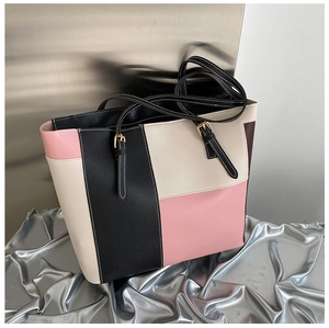Dettaglio borsa tote color-block con cuciture a contrasto e fibbie dorate su sfondo industriale