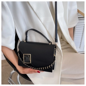 Detail of black crossbody bag with gold geometric buckle and woven chain on white suit