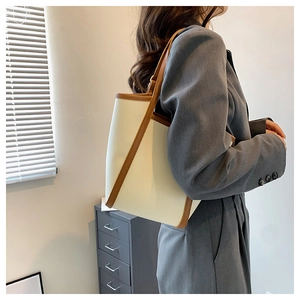 Detailed side view of off-white tote bag with brown trim worn by a model on shoulder