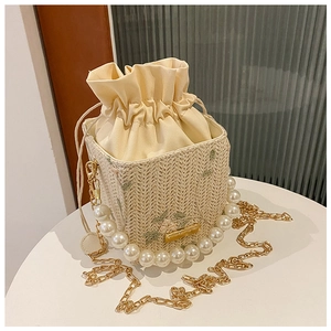 Détail du sac seau en paille avec broderie florale, anse en perles et cordon de serrage