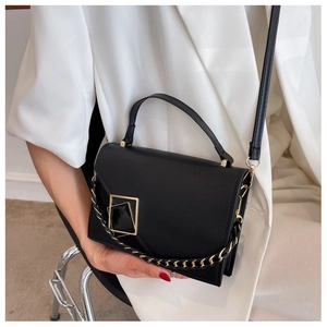 Close-up of black leather crossbody bag with gold square buckle and chain strap