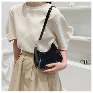 Detail of a black patent leather shoulder bag with silver hardware on a model