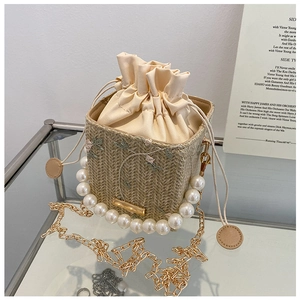 Détail du sac seau en paille avec broderie florale et élégante poignée en perles
