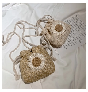 Close-up of straw bucket bag with large white daisy weave and braided shoulder strap