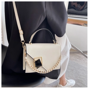 Detail view of cream crossbody bag featuring chic black edges and metal buckle on suit model