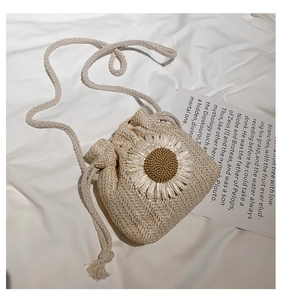 Detail of a handmade straw bucket bag with a sunflower crochet charm and drawstring closure