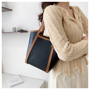 Detail of black leather tote bag with brown trim and spacious interior on shoulder