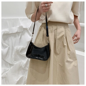 Detail shot of a black glossy patent leather shoulder bag with sleek crescent shape