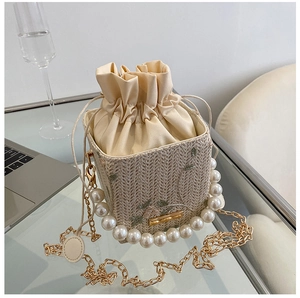 Détail du sac seau en paille avec broderie florale, anse perle et cordon en satin