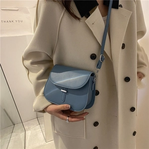 Blue minimalist saddle crossbody bag in matte leather shown on a model with a trench coat
