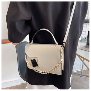 Model wearing a cream square shoulder bag with gold chain and geometric buckle