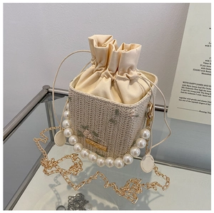 Détail du sac seau en paille avec broderie florale, anse en perles et cordon de serrage