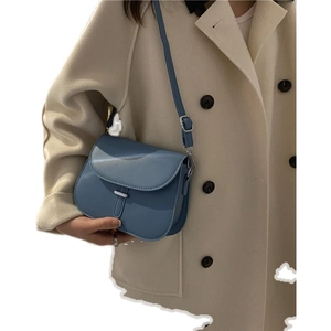 Chic smog blue saddle crossbody bag with metal buckle shown on a model's beige coat