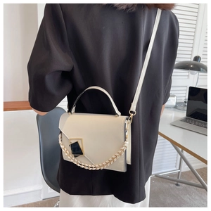 Close-up of cream crossbody bag with gold chain and geometric lock on black blazer