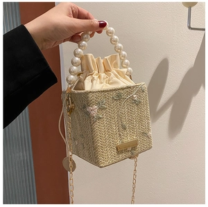 Détail du sac seau en paille avec broderie florale et élégante poignée en perles