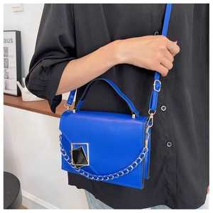 Detail of Klein blue leather handbag with gold geometric buckle and chain on model