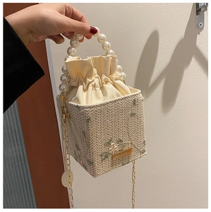 Détail du sac seau en paille avec broderie florale, anse perle et chaîne dorée