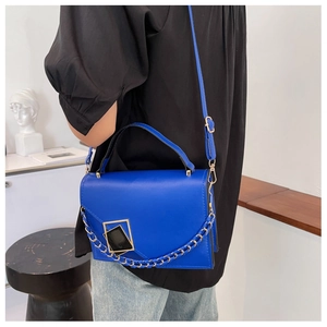 Detail of Klein Blue shoulder bag with gold chain and geometric buckle on white stand