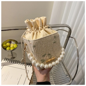 Détail du sac seau en paille avec broderie florale verte et anse en perles élégante