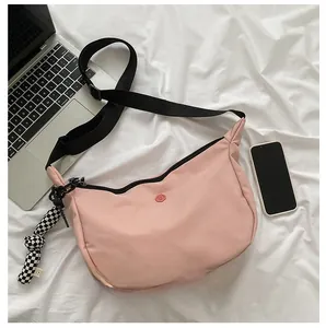 Sac bandoulière en nylon rose avec sangle noire et breloque damier sur fond blanc