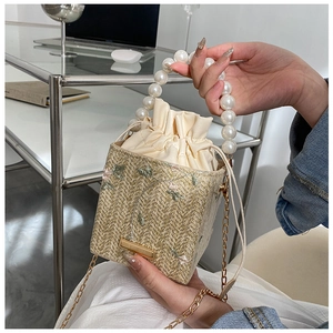Détail d'un sac seau en paille avec broderie florale et anse en perles élégante