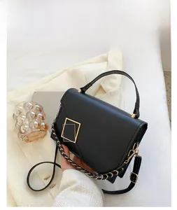 Detail of a black matte leather handbag featuring golden square metal buckles and chain strap