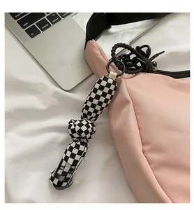 Détail du sac à bandoulière rose en nylon avec un charme à carreaux sur fond blanc