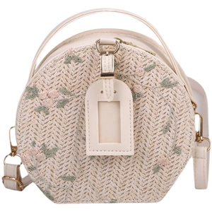 Women's round straw bag with floral embroidery and adjustable leather strap on white backdrop